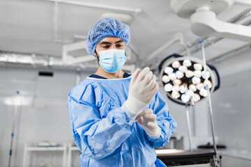 A surgeon is putting on gloves in a sterile operating room, preparing for a medical procedure.