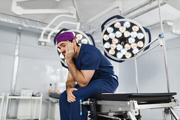 A surgeon takes a moment to rest on an operating table in a modern, well-lit operating room, surrounded by surgical lights and equipment.