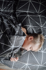 A handsome blond boy is lying in bed