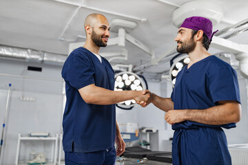 Obraz premium Two surgeons shake hands in an operating room, likely after a successful procedure or before a surgery. The scene is brightly lit.