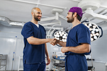 Two surgeons shake hands in an operating room, likely after a successful procedure or before a surgery.