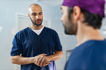 Obraz premium Two surgeons in scrubs converse in an operating room setting, likely discussing a medical procedure or patient care.