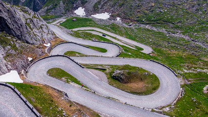 Winding Cobblestone Hairpin Road in High Alpine Pass with Green Mountains and Snow