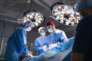 Medical team performing surgery in a modern operating room, illuminated by surgical lights.
