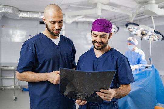 Two surgeons examine an X-ray in a modern operating room, with another medical professional in the background.