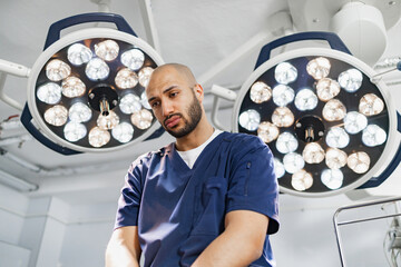 A surgeon stands under bright operating room lights, possibly contemplating a procedure.