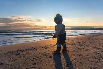 Toddler on sunrise beach. First walk by the sea.