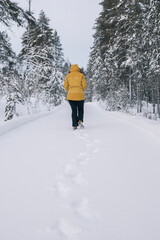 Woman walking on snowy path in a winter forest, leaving footprints in the fresh snow
