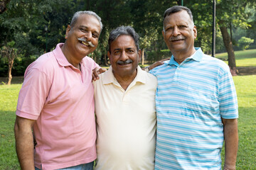 Indian happy three senior male friends standing while spending leisure time at park. Old friends wearing jacket and golf cap. Happy elderly people enjoying life after retirement.