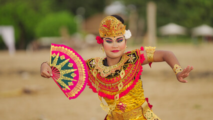 Balinese dancer performing traditional legong dance, young girl, wearing gold costume and...