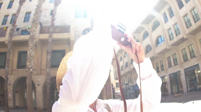 A woman takes a photo. A happy tourist. A brunette in stylish clothes poses with a camera in front of an Arab city. Adventures and travel.