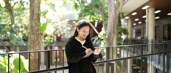 Asian high school student smiling while using a tablet while sitting outside the classroom