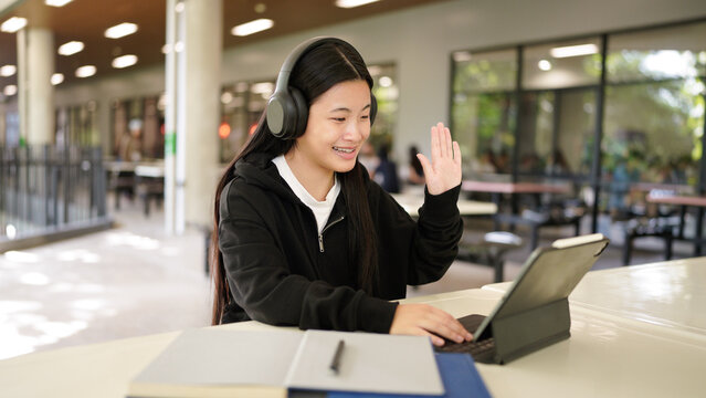 Teenage schoolgirl studying Wear headphones, using tablet , sitting in Library at school. Distance learning.