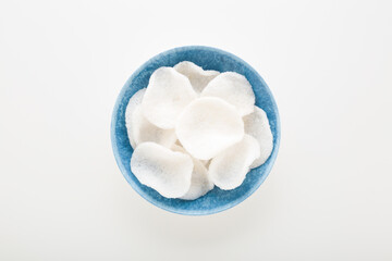 Full blue plastic bowl of white shrimp chips on light gray table background. Closeup. Top down view.