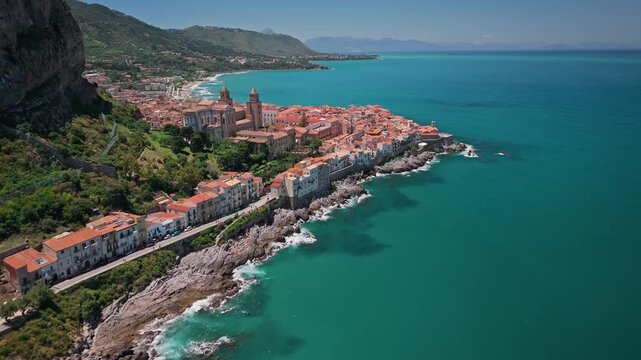 Aerial view of the Cefalu Cathedral and the town's terracotta rooftops meeting the turquoise sea, a vibrant contrast of color and texture, Cefalu, Sicily, Italy.