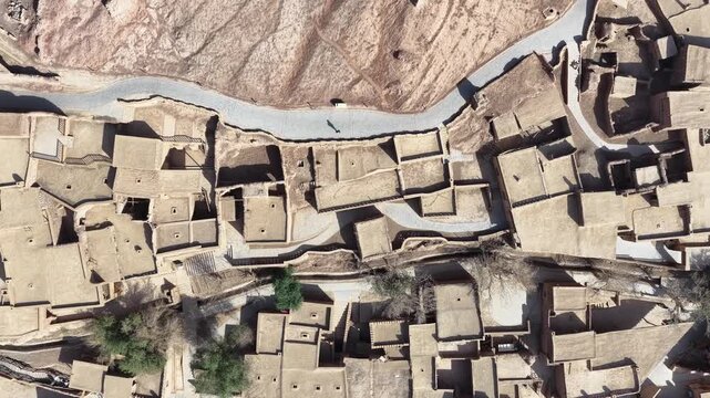 Aerial view of the ancient Tuyugou Xia Village reveals traditional mud-brick houses nestled between a winding road and arid landscape, Tuyugou Xia Village, China.