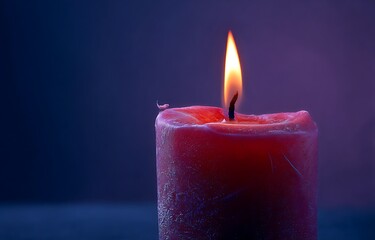 Close-up of red candle burning on dark blue background, close up of red lit candle flame