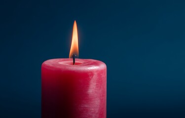 Close-up of red candle burning on dark blue background, close up of red lit candle flame