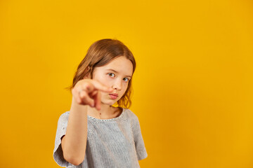 Child making a finger-pointing gesture against a bright yellow background during a playful moment