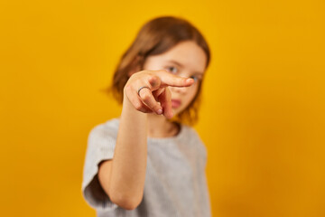 Child making a finger-pointing gesture against a bright yellow background during a playful moment