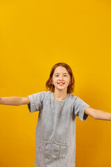 Cheerful girl giving thumbs up with open arms against a bright yellow background