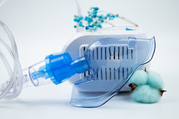 Close-up side view of a home inhaler with a blue mask and a machine on a white background and blue...
