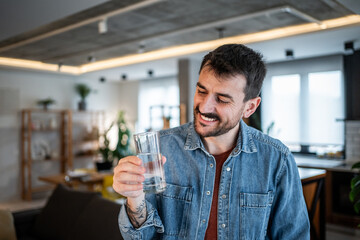 Young man holding glass of water looking happy staying hydrated