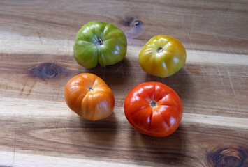 Home grown organic beef tomatos at different stages of ripening on wooden board