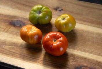 Home grown organic beef tomatos at different stages of ripening on wooden board