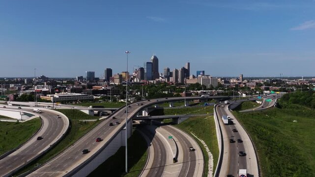 Drone ascends over interchange to reveal downtown Indianapolis skyline on summer day.