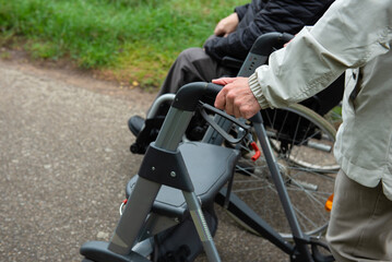 Obraz premium Elderly friends taking a walk in the park during cold weather with help of wheelchair and walker enjoying and having fun