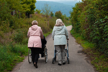 Elderly people taking a walk with help of walker with friends on a cold day through the park 