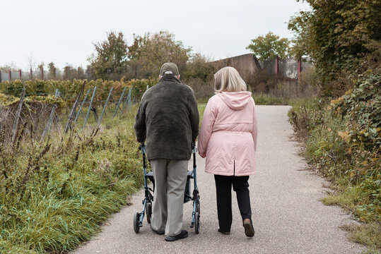Elderly people taking a walk with help of walker with friends on a cold day through the park - Powered by Adobe