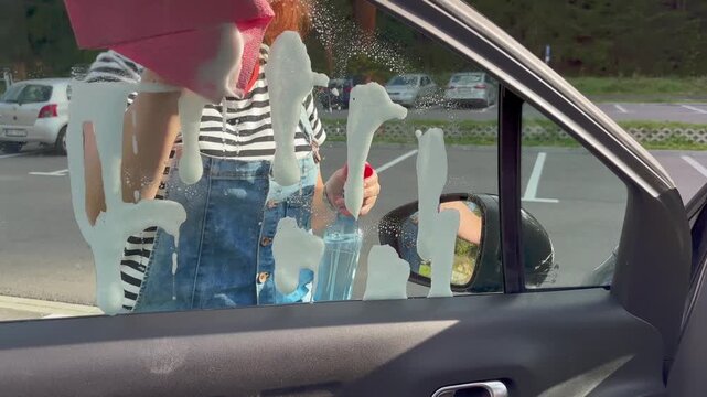 Woman cleaning a car window on a parking in a sunny day