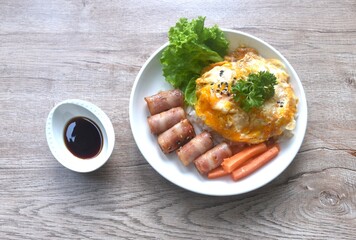 fried creamy egg omelet topping plain rice with pork bacon roll sausage and carrot dipping Japanese teriyaki sauce on plate 