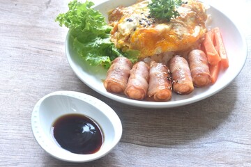 fried creamy egg omelet topping plain rice with pork bacon roll sausage and carrot dipping Japanese teriyaki sauce on plate 