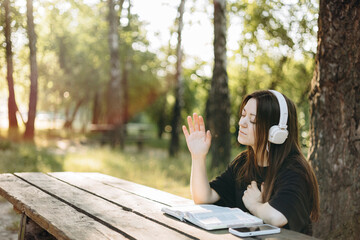Young teen girl in headphones reading the Bible at a wooden table outdoors.
