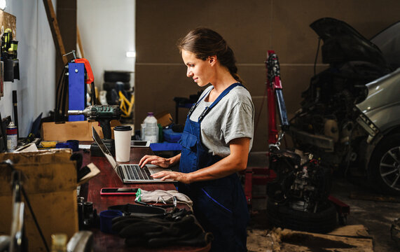 Female auto mechanic working on laptop in local car repair garage.