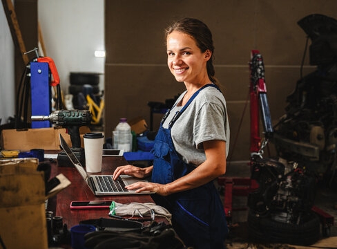 Female auto mechanic working on laptop in local car repair shop.