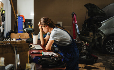 Worried woman entrepreneur in car service shop having business difficulties. Bankruptcy of a small business.