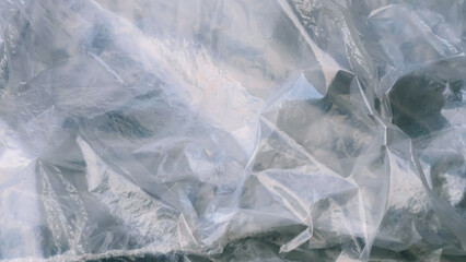 Close-up of crumpled, translucent plastic material, creating abstract patterns of light and shadow.