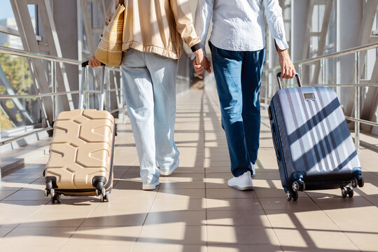 Closeup of mature travelers holding hands while pulling suitcases at airport