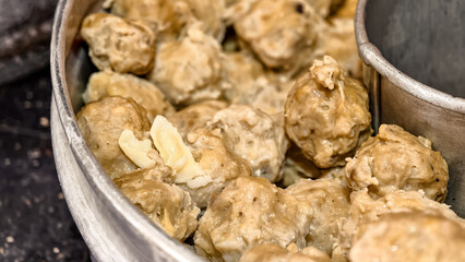 Close-up of cooked meatballs in a metal container, some with visible pieces of garlic.