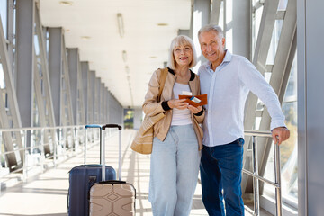 Smiling mature couple standing at airport with luggage and passports