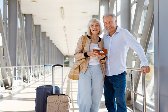 Smiling mature couple standing at airport with luggage and passports