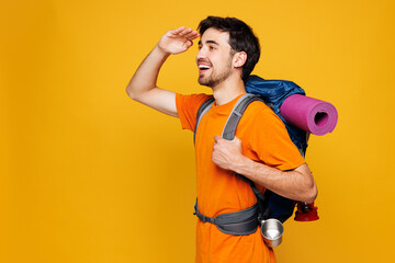 Young fun traveler man carry backpack with stuff mat look far away isolated on plain yellow...