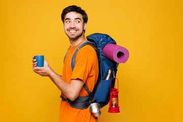 Young traveler man carry backpack with stuff mat hold cup drink coffee tea isolated on plain yellow...