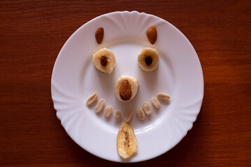 Creative fruit art featuring smiling face made of bananas and nuts on a white plate for playful snack time