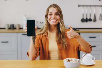 Young happy housewife woman wear orange shirt casual clothes hold in hand use blank screen mobile...
