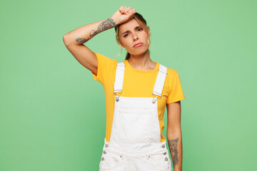 Young sad sick ill woman she wears yellow t-shirt overall casual clothes put hand on forehead suffer from headache isolated on plain pastel light green background studio portrait. Lifestyle concept.